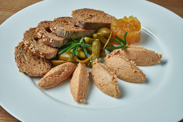 Appetizing antipasti - goose paste with jam, rosemary and rye bread in white plate on wooden background/