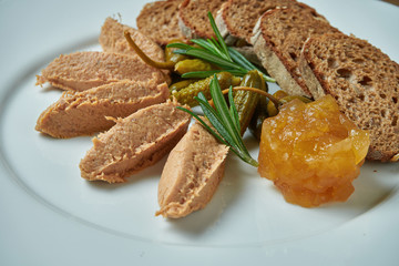 Appetizing antipasti - goose paste with jam, rosemary and rye bread in white plate on wooden background/