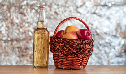 Basket with red fresh apples and a bottle of cider on a wooden table.