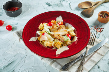 Tasty Caesar salad with chicken, croutons, parmesan, cherry tomatoes and lettuce in a white plate on a gray background