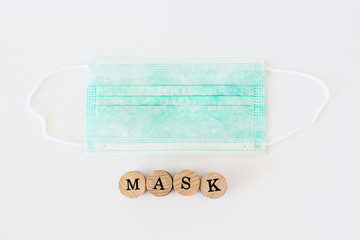 Word mask written with wooden blocks with black letters laying on protective surgical masks, flat lay concept