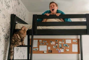 A guy under a blanket on a bunk bed yawns with the cats