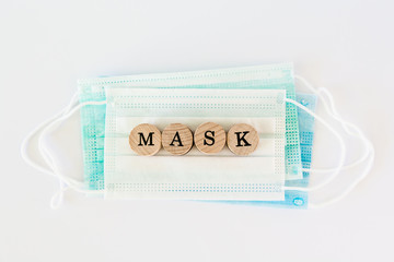 Word mask written with wooden blocks with black letters laying on protective surgical masks, flat lay concept
