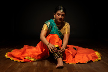 Kathak dancer tying ghungroo in her ankles. 
