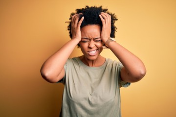 Young beautiful African American afro woman with curly hair wearing casual t-shirt suffering from headache desperate and stressed because pain and migraine. Hands on head.