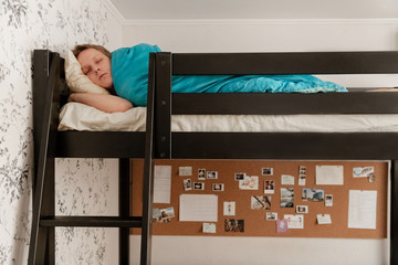 Fototapeta na wymiar The guy is sleeping on a bunk bed under a blue blanket