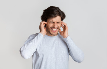 Ear pain concept. Guy grimaces and touches ears