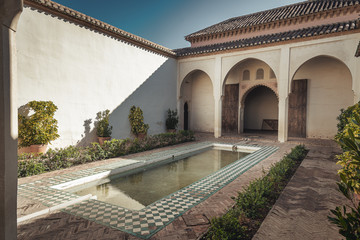Alcazaba interior courtyard with pool and covered walkway and columns and arches from moorish islamic architecture in Malaga Spain with plants, daylight with shadows.