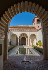 Alcazaba arabic arch interior courtyard with pool and covered walkway and columns and arches from moorish islamic architecture in Malaga Spain with plants, daylight with shadows.