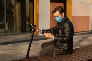 man wears protective mask against infectious diseases and flu sitting on street in city with electric scooter. coronavirus quarantine.