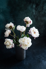 Bouquet of fresh white peonies in a grey vase on a dark background. 