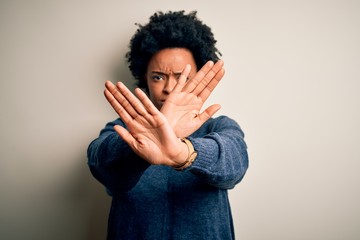 Young beautiful African American afro woman with curly hair wearing casual sweater Rejection expression crossing arms and palms doing negative sign, angry face