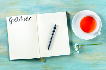 Gratitude journal with a pen, a flower, and a cup of tea, shot from above, with the handwritten word