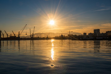 Backlit sunset in the port of Malaga with cranes and the sun reflecting in the sea water.