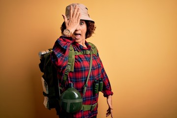 Middle age curly hair hiker woman hiking wearing backpack and water canteen using binoculars...