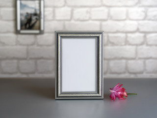 An empty, beautiful photo frame and a pink flower against a gray brick wall. Mock-up. Stylized stock photos.