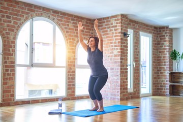 Middle age beautiful sportwoman smiling happy. Standing on mat practicing yoga doing chair pose at gym