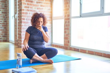 Middle age beautiful sportswoman wearing sportswear sitting on mat practicing yoga at home feeling unwell and coughing as symptom for cold or bronchitis. Healthcare concept. - obrazy, fototapety, plakaty