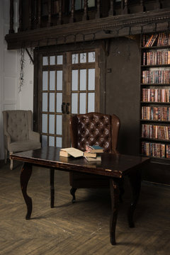 Classical library room with leather armchair, wooden table and bookcase..