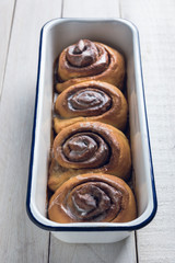 Fresh homemade cinnamon rolls on a baking pan, over a white rustic wooden table. From above with selective focus.