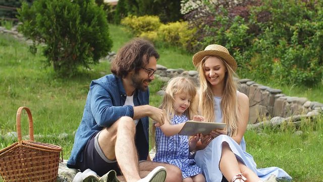 Happy caucasian Family sitting in garden watching tablet. Family vacation concept.