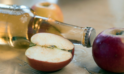 A bottle of apple cider lies on the table with apples. Soft focus concept