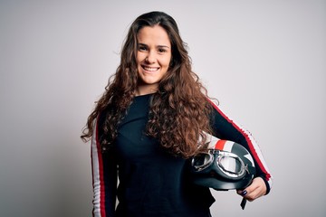 Beautiful motorcyclist woman with curly hair holding moto helmet over white background with a happy face standing and smiling with a confident smile showing teeth