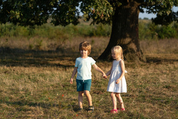 Naklejka na ściany i meble Happy little couple holding hands on field background. Children holding hands. Summer in love.