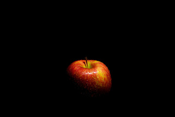 Ripe juicy red and green autumn apple in water drops and spray on a black background