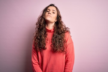 Young beautiful woman with curly hair wearing turtleneck sweater over pink background Relaxed with serious expression on face. Simple and natural looking at the camera.