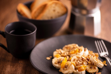 plate with sliced banana with granola, candied fruit and honey, toast and a cup of coffee