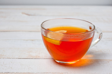 Glass cup with tea and lemon standing on a white painted wooden surface. Background for hot drinks. Soft and tonic drinks.