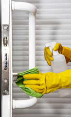  hand in yellow rubber household gloves cleans door handle using wipe and bottle of cleaning spray
