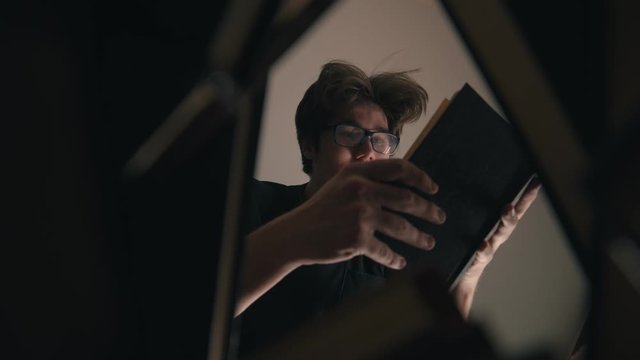 A young smiling man in glasses picking up books from the floor