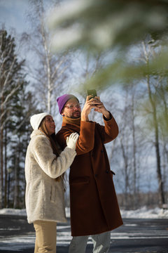 young couple in winter park shooting pictures with mobile phone
