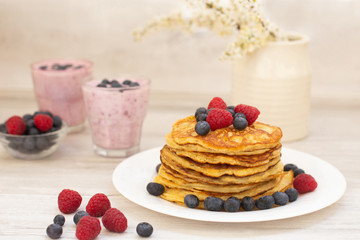 Pancakes with blueberries, 
raspberries and tasty 
berry smoothies for breakfast. Plate of homemade pancakes with forest berries on wooden table   
