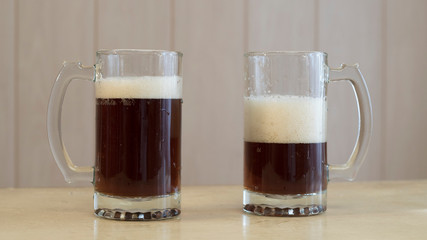 Two glass mugs with dark and beer on the table.