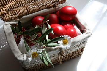 Rote Ostereier in geflochtenem Korb mit Blüte und Olivenblättern als Dekoration