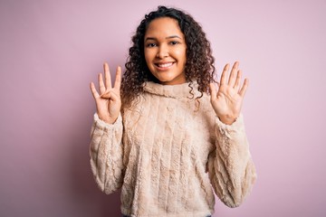 Young beautiful woman with curly hair wearing casual sweater standing over pink background showing...
