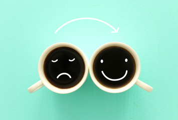 unhappy and happy  faces over coffee cups. concept of mindset and emotions