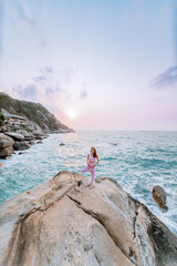 Fototapeta na wymiar Pregnant woman practices yoga, standing in vrksasana position on the beach, on the rocks. Hands of girl in a pose meditating. Serenity practicing at sunrise, meditation. Woman in pink-purple tracksuit