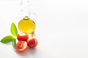 on a white background vegetable olive oil in a glass decanter. Nearby are slices of tomatoes and a green leaf.