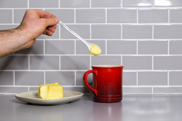 Mans hand holding a teaspoon of butter with a red coffee mug to make bulletproof coffee.