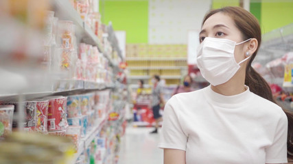 Asian girl wearing a mask While choosing to buy instant noodles to hoard Keep for eating during the Coronavirus epidemic. © sunchai
