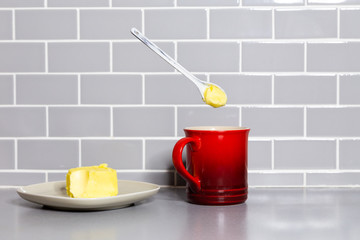 A floating teaspoon of butter with a red coffee mug to make bulletproof coffee.