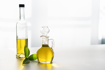 against the window, olive oil in a decanter and in a glass bottle, with a green leaf