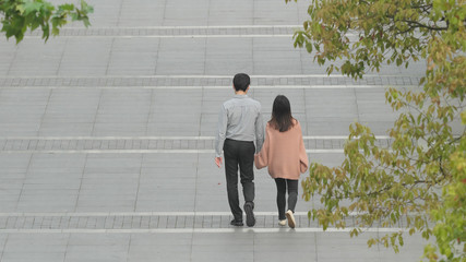 High angle view of lovers walking side by side on road, rear view of  young man and woman walking hand in hand.