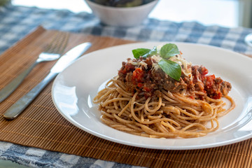 
wholemeal spaghetti pasta with bolognese sauce and basil on a white plate