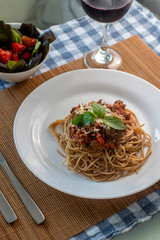 
wholemeal spaghetti pasta with bolognese sauce and basil on a white plate