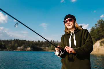 Woman catching a fish, pulling rod while fishing on lake or pond at the weekend. Fisherman with rod, spinning reel on the river bank. Sunrise. Fishing for pike, perch, carp. Background wild nature.